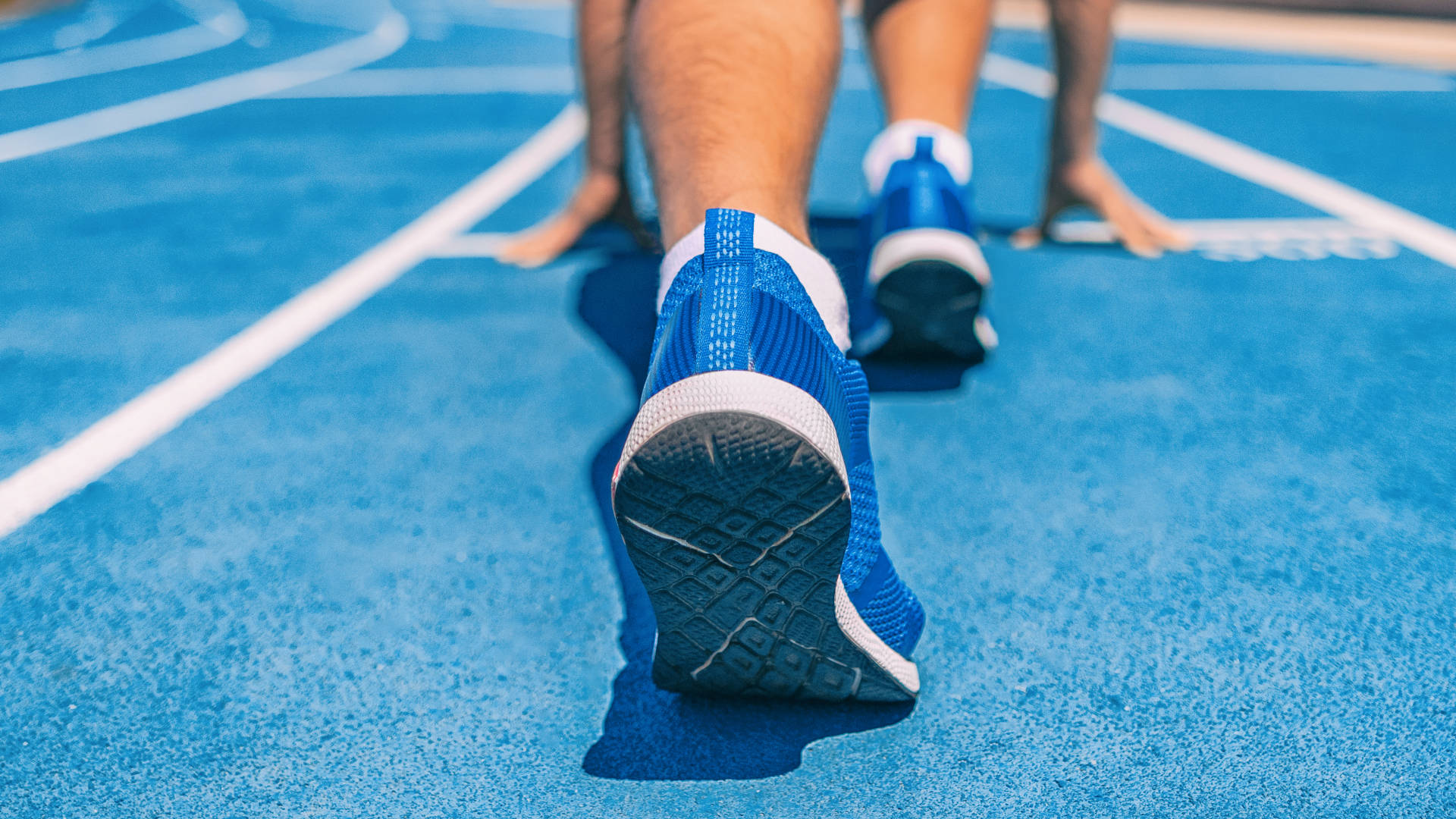 A view of a runner at the starting line of a race on a track. The perspective is from about a meter behind their shoes and only encompasses their trainers